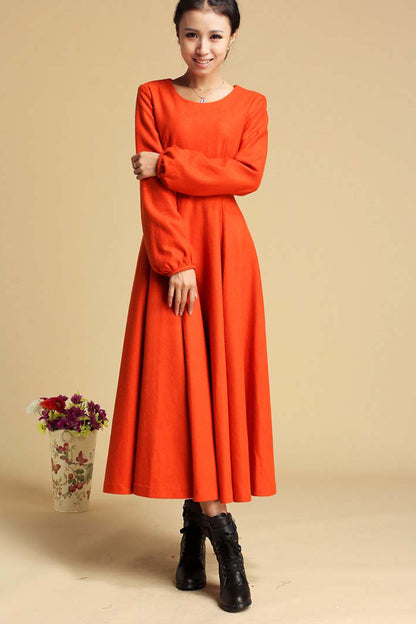A woman wearing an orange maxi dress with long sleeves, a round neckline, and a zipper on the right side. The dress has a regular fit and is paired with black boots.