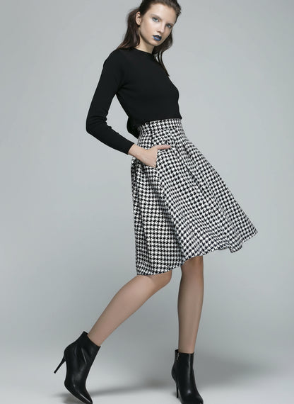 Woman wearing a black top and houndstooth patterned skirt on a gray background
