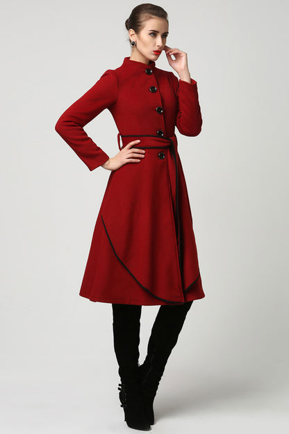 A woman modeling a long red cashmere coat with oversized button closure and a self tie belt waist, falling just below the knee.