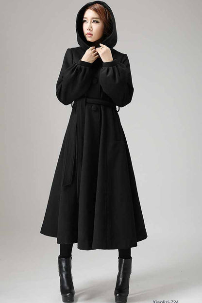 A woman wearing a black wool coat with long lantern sleeves, a hood, and a tie belt waist. The coat is displayed on a plain background.