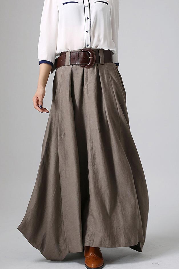 A woman wearing a gray linen maxi skirt with side pockets, paired with a white top and accessorized with a brown belt and accessories.