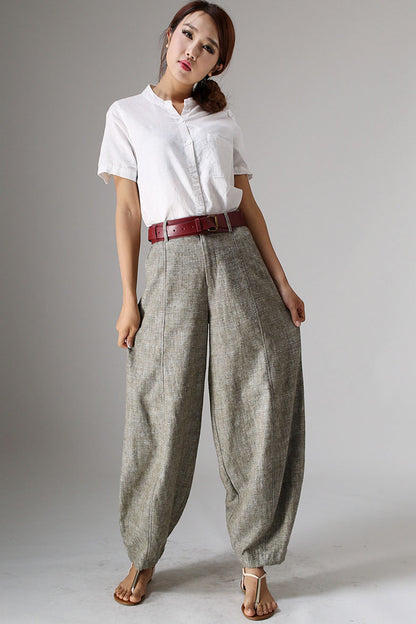 A woman standing, wearing baggy linen pants with pockets on the sides and a red belt.