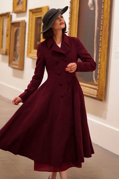 A woman wearing a wine red long princess wool coat with a wide-brimmed hat, double-breasted button closure, and two side seam pockets, standing in a museum with paintings in the background.