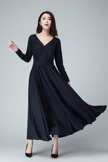 A woman modeling a navy blue, V-neck, long-sleeve linen dress with a fit and flare silhouette, featuring pleated detailing on the shoulders and waist.